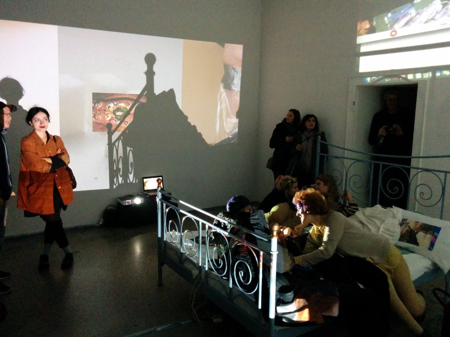 Exploit & Disappear — visitors around the bed, projector beam and projections