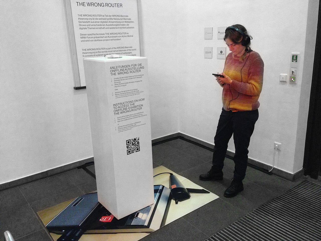 The Wrong Router — a visitor with headphones using a phone beside the plinth